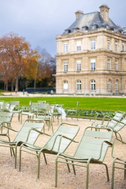Lüksemburg Bahçeleri, Paris, Fransa 'da çakıl yolunda birden fazla açık yeşil metal sandalye. Lüksemburg Sarayı bulutlu bir sonbahar gününde arka planda görünür..