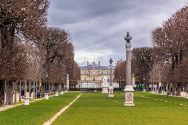 Arka plandaki Lüksemburg Sarayı 'na giden çıplak ağaçlardan ve süslemelerden oluşan bir ara sokak. Fransa 'nın Paris kentindeki Lüksemburg Bahçeleri' nde bulutlu bir günde tanınmayan insanlar yürüyor..