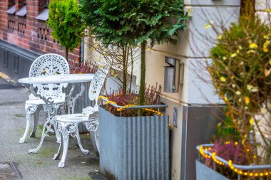 Almanya 'nın kuzeyinde, ortaçağ Lubeck, Holstein eyâletinde, binalar ve sonbahar yapraklarıyla birlikte tarihi bir kaldırımda metal bir zincirle zincirlenmiş eski tip demir masa ve sandalyeler..