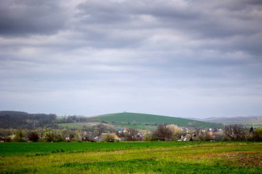 Ukrayna 'nın Cherkasy bölgesindeki Mliyiv köyünün tarihi bir simgesi olan Kozatska Mohyla Tepesi manzarası. Fotoğraf, ön planda haçlı bir tepe ve yeşil bir tarla gösteriyor. Baharın sonlarında, nisan sonunda..