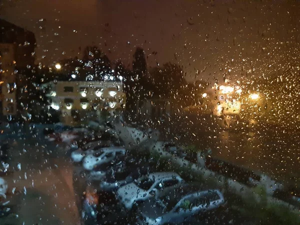 Nedves esőüveg esténként az udvar hátterében autókkal — Stock Fotó