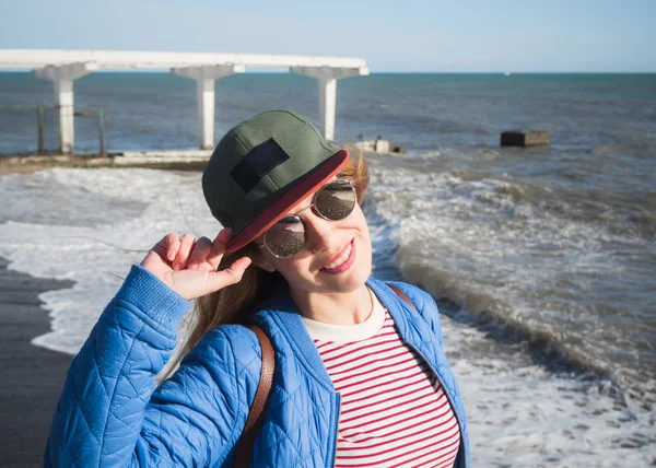 Όμορφο κορίτσι στα γυαλιά ηλίου κρατά ένα καπάκι στη θάλασσα — Φωτογραφία Αρχείου