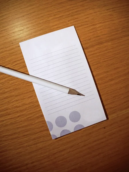 Lápis branco e folha de caderno deitado em uma mesa de madeira — Fotografia de Stock