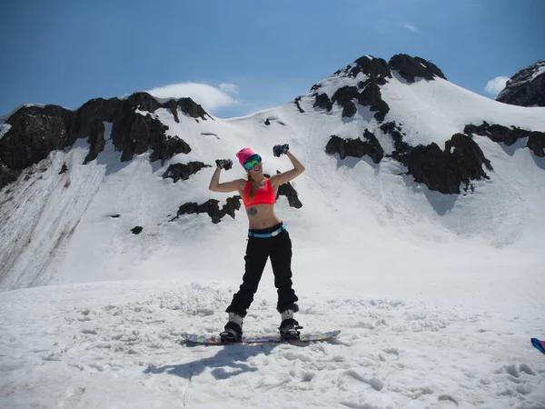 Όμορφο κορίτσι χιονοοικότροφος που παρουσιάζουν τη δύναμη των δικέφαλων στο φόντο των βουνών στο χιονοδρομικό θέρετρο Γκόρκι-Γκορόντ. Ρωσία Σότσι 05.11.2019 — Φωτογραφία Αρχείου