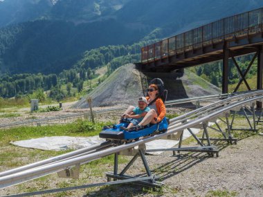Neşeli anne ve oğlu Rodelbahn binmek. Rosa Khutor. Yükseklik 1100 m. Rusya Soçi 08 04 2019
