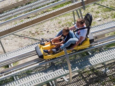 Ağabeyi ve küçük kardeşi Rodelbahn geri yüksek hızda saçlarını binmek. Rosa Khutor. Yükseklik 1100 m. Rusya Soçi 08 04 2019