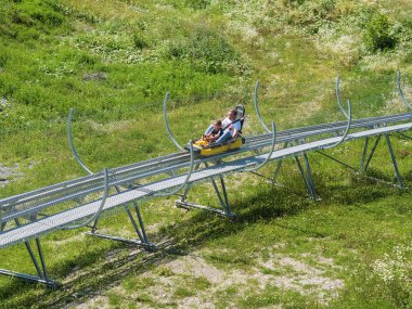 Ağabeyi ve küçük kardeşi Rodelbahn geri yüksek hızda saçlarını binmek. Rosa Khutor. Yükseklik 1100 m. Rusya Soçi 08 04 2019