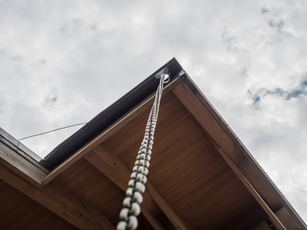 A long chain hangs from the corner of the roof of a house amid clouds