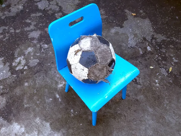 Una pelota de fútbol desaliñada yace en una silla para niños en el patio de la calle. Triste infancia —  Fotos de Stock