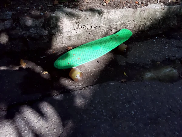 Skateboard hijau berdiri di sebuah jalan di halaman diterangi oleh sinar matahari yang indah — Stok Foto