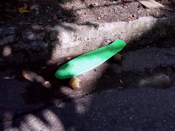 Green skateboard stands on a street in the courtyard lit by beautiful sunlight