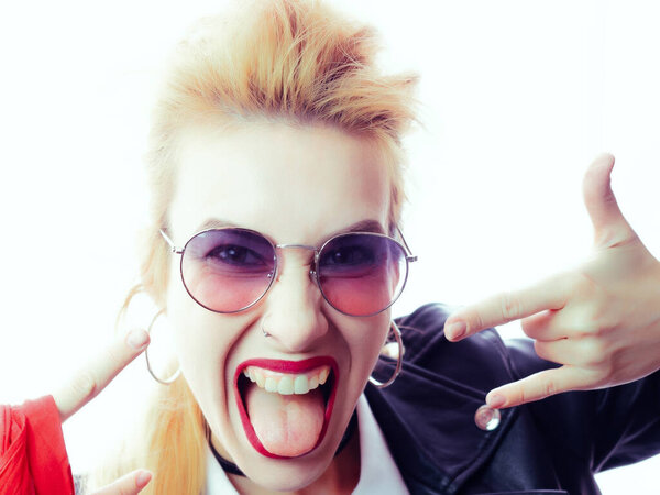 Beautiful girl in black leather jacket and sunglasses shows tongue and hand gesture rock