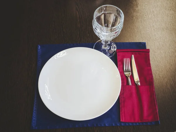玻璃和银器的白色陶瓷盘躺在木制表面的餐巾纸上。表格设置 — 图库照片