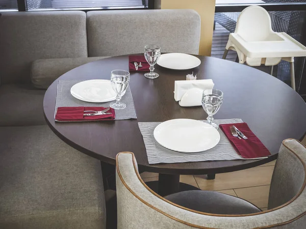 Op een ronde tafel staan bestek voor drie personen, naast een zachte grijze bank en fauteuil — Stockfoto