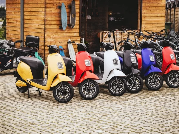 Rusya, Soçi 14.03.2020. Birçok renkli elektrikli motosiklet ahşap bir evin arka planına karşı kaldırım taşları üzerinde bir sırada durur. Motosiklet kiralama — Stok fotoğraf