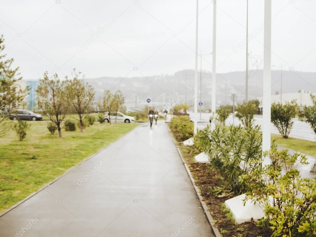 Sidewalk with two people riding in the distance on electric scooters in cloudy weather. Blurred effect