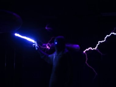 Karanlıktaki bir adamın bulanık çizgisi eliyle dev parlak bir yıldırıma dokunuyor. Odaklanmayın