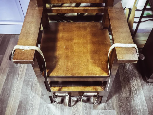 Old wooden chair with shabby leather straps attached to the armrests and legs. Chair for torture. Antique electric chair. Museum exhibit