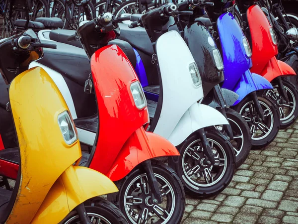 Çok renkli elektrikli motosikletler kaldırım taşlarının üzerinde duruyor.