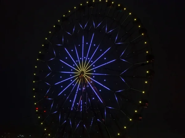 Night photo high modern ferris wheel with a bright pattern of blue and yellow lights glowing in the dark — Stock Photo, Image