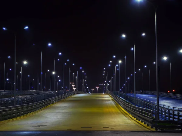 Geniş sarı yolun gece görüşü. Yan taraftaki fenerlerle aydınlatılıyor. — Stok fotoğraf