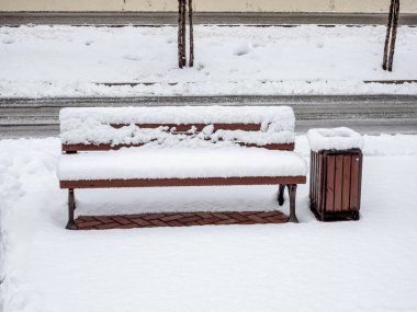 Bir bank ve çöp tenekesi dışarıda duruyor. Taze beyaz karla kaplı.