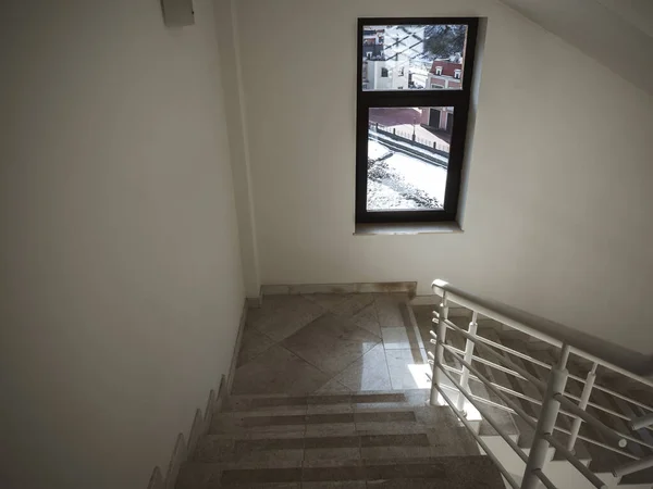 Couloir blanc avec marches en marbre beige, balustrades blanches et fenêtre encadrée noire. — Photo