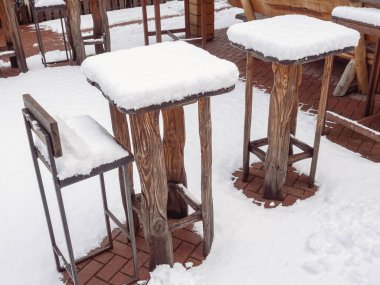 Uzun ahşap masalar ve kışın karla kaplı bir kafenin bar taburesi.