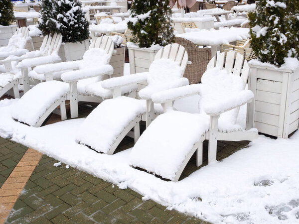 Wooden white sun chairs stand in a row strewn with snow