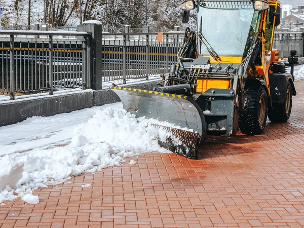 Traktor odstraňuje sníh z dlažebních desek podél černého kovového plotu na ulici — Stock fotografie