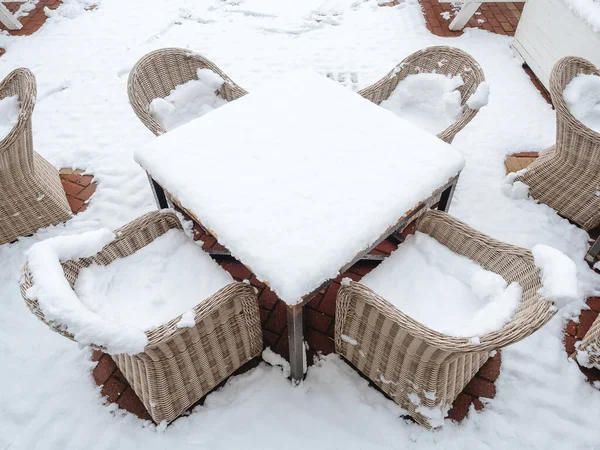 Wicker chairs strewn with snow stand around a snow-strewn table on a snow-covered area — Stock Photo, Image