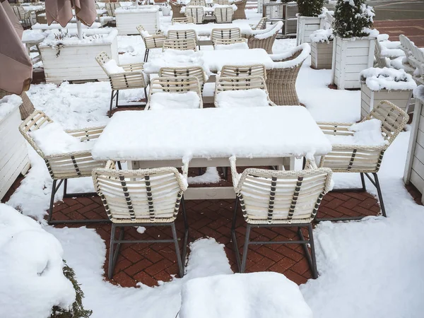 Café callejero con mesas, sillas, sombrillas y macetas de madera con arbustos completamente cubiertos de nieve fresca —  Fotos de Stock