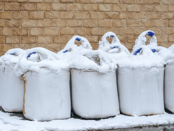 White bags with snow-covered tops stand against a wall with brickwork — Stock Photo, Image