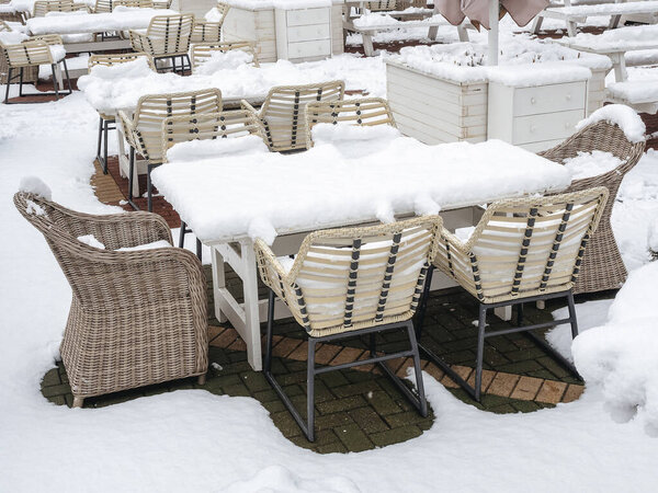 Street cafe with wooden tables and wicker chairs and armchairs strewn with snow