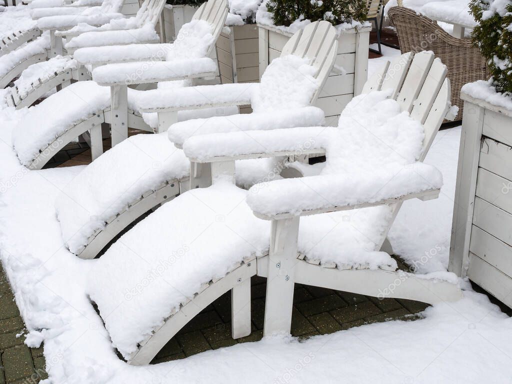 White wooden sun loungers stand covered with snow