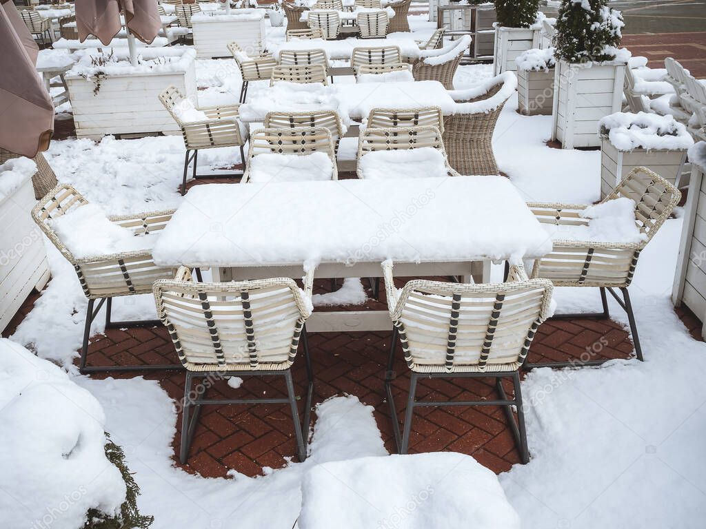 Street cafe with tables, chairs, umbrellas and wooden pots with bushes completely covered with fresh snow