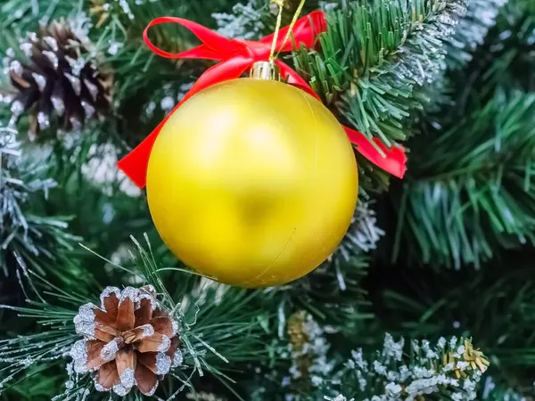 Золотой матовый рождественский бал, висящий на искусственной сосновой ветке с настоящими шишками — стоковое фото