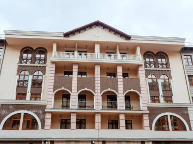 Kemerli camları, balkonları ve üçgen çatısı olan bej kahverengi bir bina.