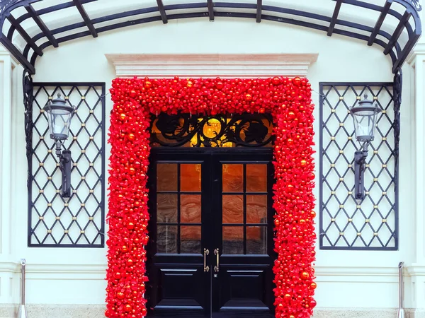 Entrance to the building with black doors with glass and red New Years decor around the doors and with lamps on decorative grilles on the sides