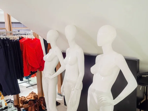 Tre vita nakna kvinnliga skyltdockor står mot en vägg i en butik mot en bakgrund av hängande kläder — Stockfoto