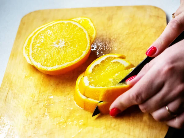 Womens hands with red nails cut an orange on the cutting board — Stock Photo, Image