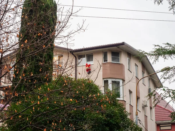 A beige house with Santa Claus hanging from a window stands among green trees and with fallen leaves. — Stock Photo, Image