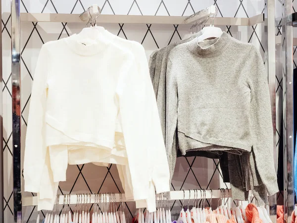 Grå och vita tröjor hänger på galgar i butiken — Stockfoto
