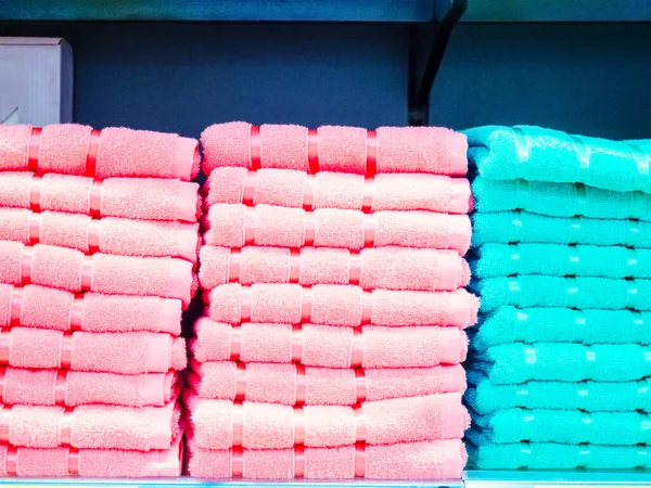 Pilhas de toalhas terry rosa e turquesa são empilhadas em uma prateleira em um fundo azul — Fotografia de Stock