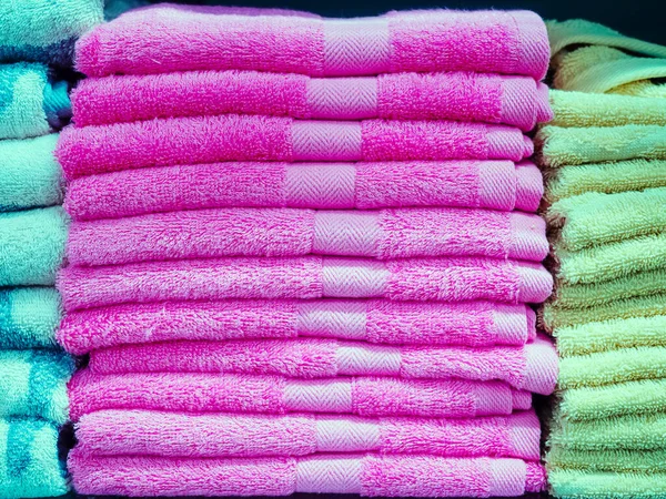 Uma pilha de toalhas terry idênticas cor-de-rosa no meio e toalhas turquesa e verde nas laterais — Fotografia de Stock