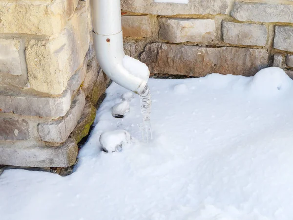 Istapp hängande från ett avloppsrör ovanför snön mot en stenmur — Stockfoto