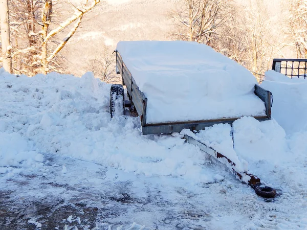 En vagn fylld med snö står i en snödriva mot en bakgrund av skogsklädda berg och träd — Stockfoto