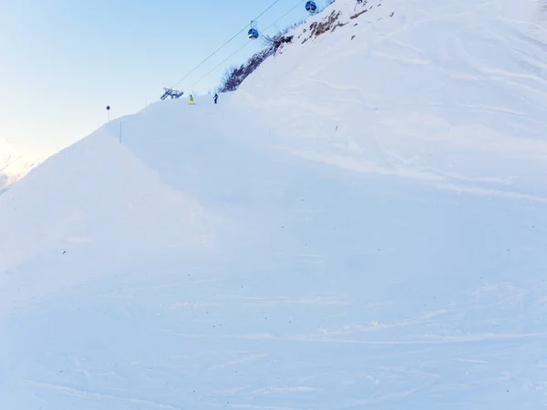 Pistas de esqui cobertas de neve com snowboarders caindo na distância e um elevador de handebol no topo — Fotografia de Stock