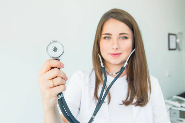 Blurred Young smiling female doctor holding her stethoscope to insinuate that it\'s time for a check up in clinic on white background. Selective focus on phonendoscope. Copy space