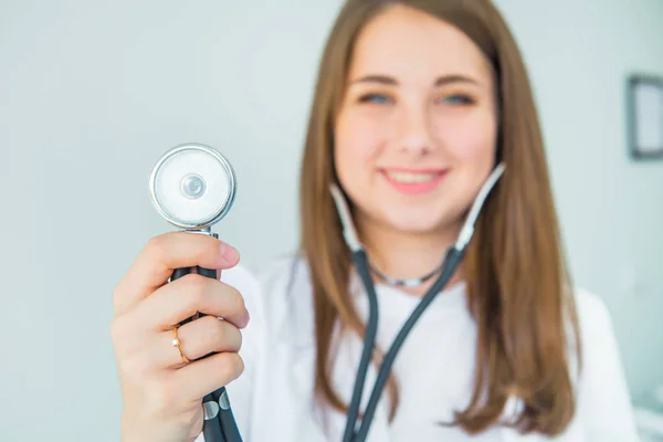 模糊的年轻微笑的女医生拿着听诊器暗示 是时候在诊所里用白色背景进行检查了 选择性地专注于音镜 复制空间 — 图库照片